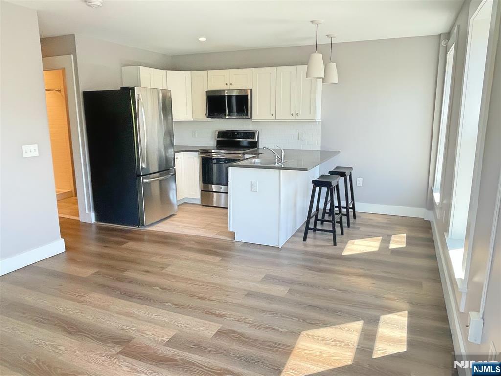 a kitchen with a refrigerator a microwave a stove and white cabinets with wooden floor