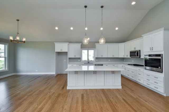 a large kitchen with kitchen island a stove a sink dishwasher a refrigerator white cabinets and wooden floor