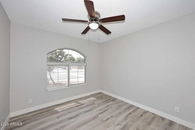 an empty room with wooden floor ceiling fan and windows