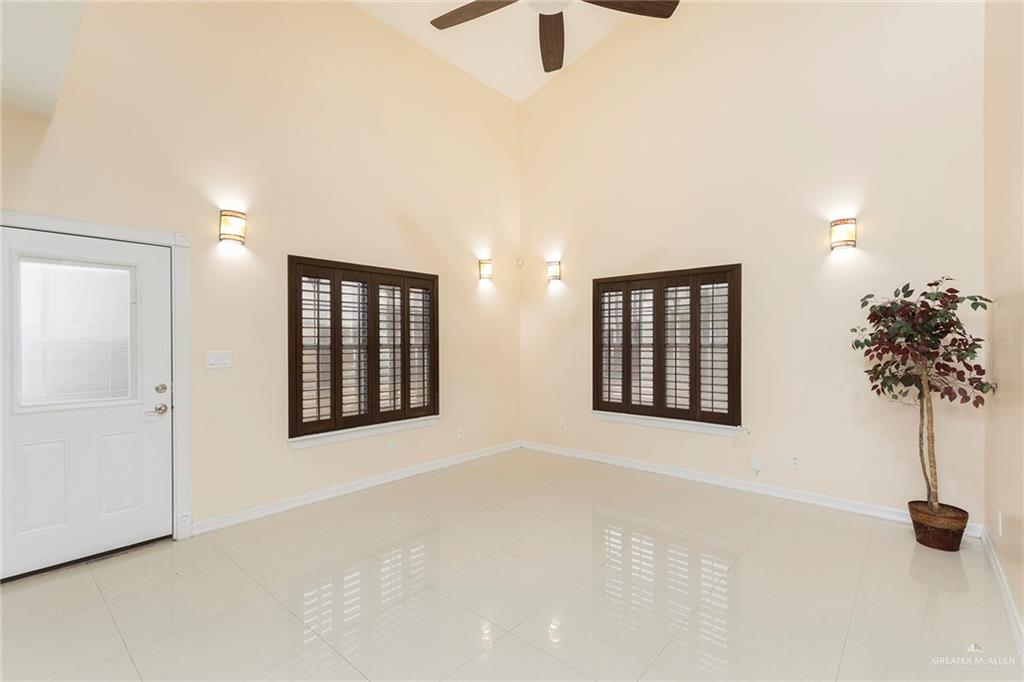 2001 Quail Lane Mission, TX 78572 - Photo 10 of 28 Vaulted ceiling with a ceiling fan, light-colored tile flooring, two windows with dark wood plantation shutters, and wall-mounted sconce lighting