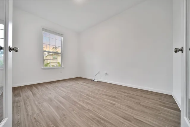 a view of an empty room with wooden floor and a window