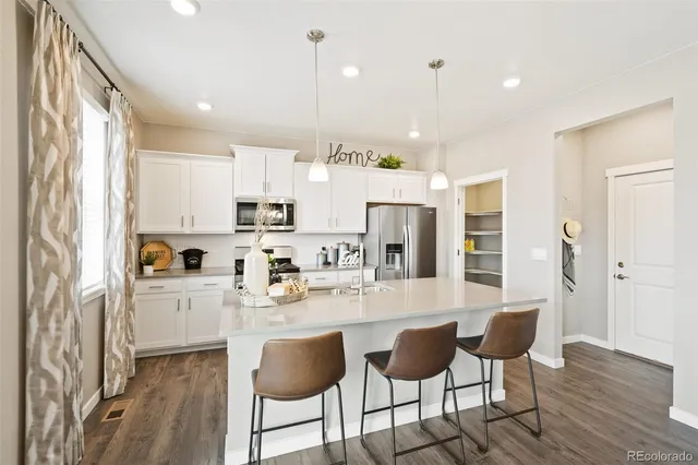 a kitchen with stainless steel appliances kitchen island granite countertop a refrigerator a stove a sink dishwasher and white cabinets with wooden floor