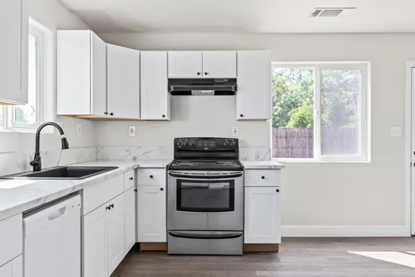 a kitchen with stainless steel appliances granite countertop white cabinets a stove a sink and dishwasher