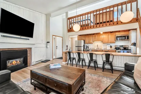 a living room with stainless steel appliances a fireplace a flat screen tv and kitchen view