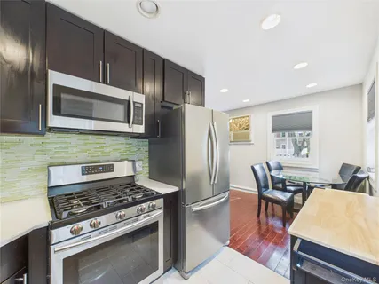 a kitchen with stainless steel appliances a stove a microwave a sink a refrigerator white cabinets and wooden floor