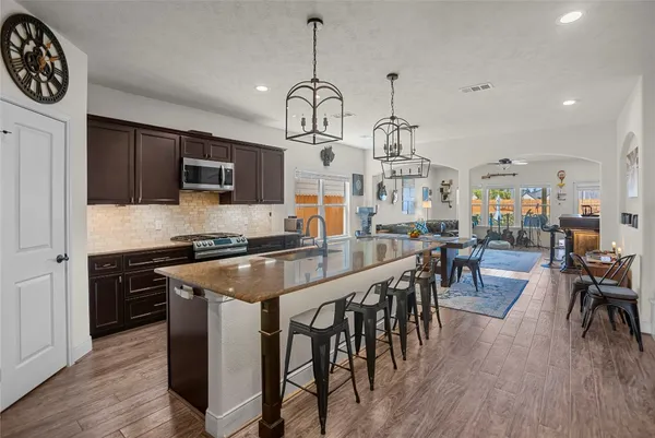 a kitchen with stainless steel appliances granite countertop a stove a refrigerator a kitchen island a dining table and chairs with wooden floor