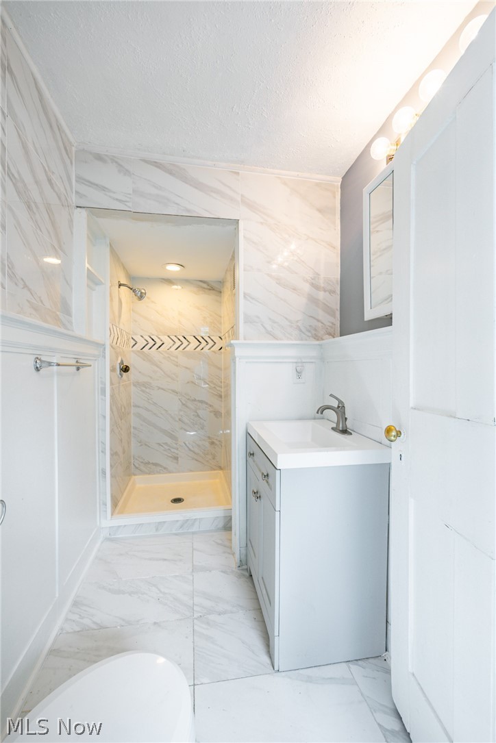 39016 Detroit Road Avon, OH 44011 - Photo 16 of 36 Bathroom featuring tile walls, large vanity, tile flooring, a textured ceiling, and tiled shower