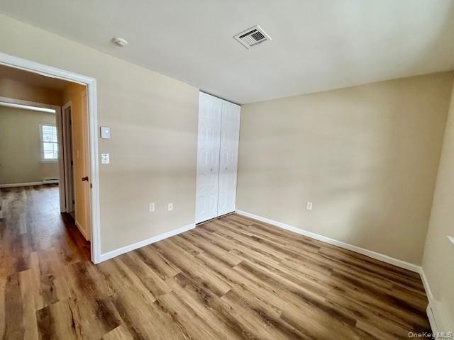 373 Woodbridge Drive, Unit B Ridge, NY 11961 - Photo 18 of 25 Unfurnished bedroom with New wood finished floors, a closet, and a baseboard radiator