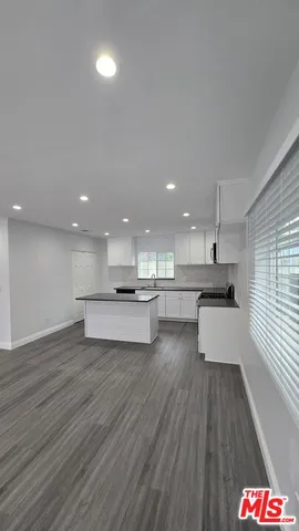 a view of an empty room with wooden floor and a kitchen