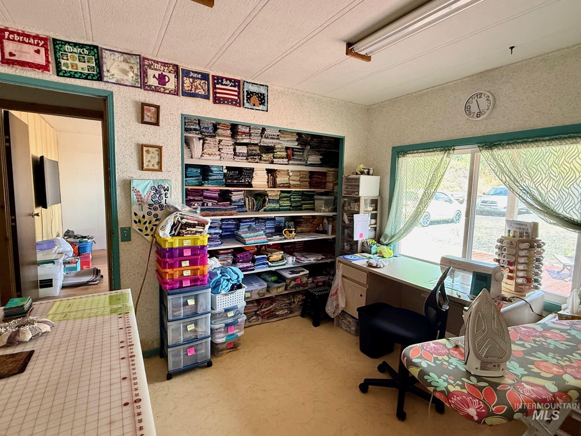 35322 River Road Lenore, ID 83541 - Photo 22 of 42 Room featuring a large window with green patterned sheers, built-in shelving, a fluorescent ceiling light fixture, and a neutral-toned floor