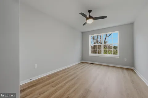 an empty room with wooden floor ceiling fan and windows