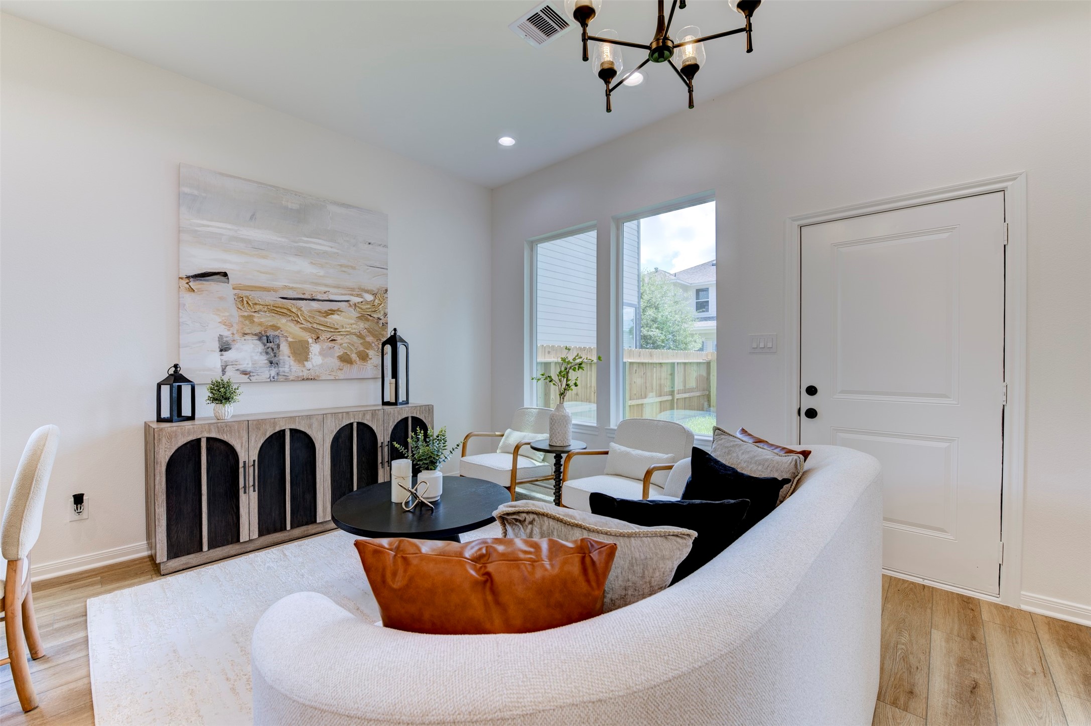 6807 Paris Street Houston, TX 77021 - Photo 11 of 50 Living room detail showing hardwood floors, matte black chandelier, recessed lighting, large rear-facing windows with yard view, rear exit door, and open layout with clear sightline through the space.