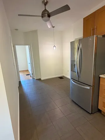 a view of a refrigerator in kitchen and an empty room with wooden floor