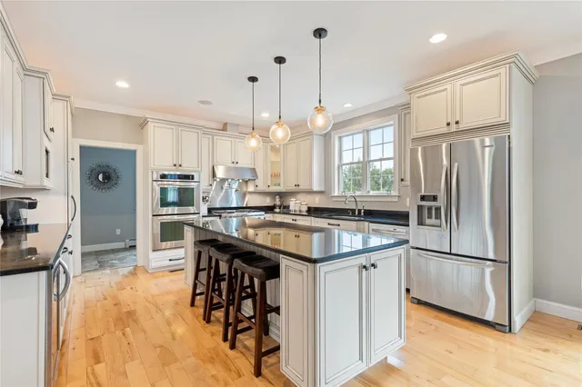 a kitchen with stainless steel appliances granite countertop a sink a stove a refrigerator and island with wooden floor