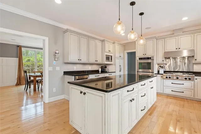 a kitchen with stainless steel appliances kitchen island granite countertop a stove a sink a refrigerator and white cabinets with wooden floor