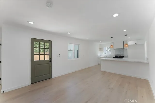 a view of an empty room with kitchen and window
