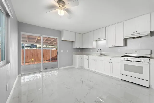 a kitchen with granite countertop a stove a sink and white cabinets