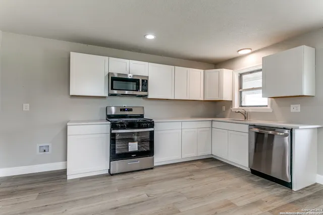 a kitchen with granite countertop a stove top oven a sink dishwasher and a microwave oven on the wooden floor