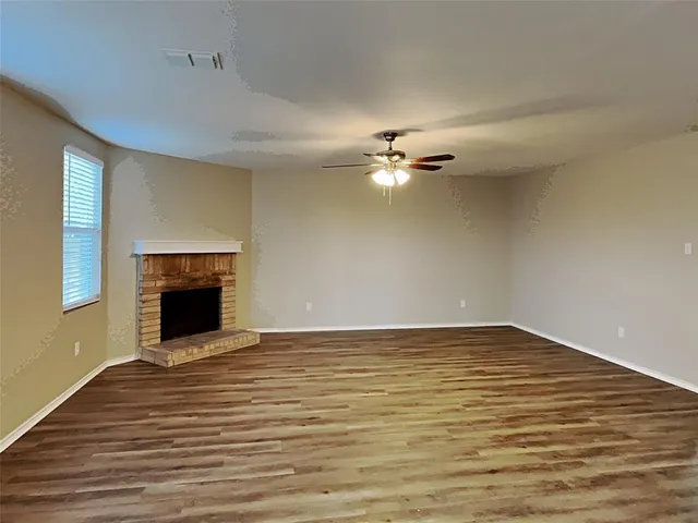 a view of an empty room with wooden floor fireplace and a window