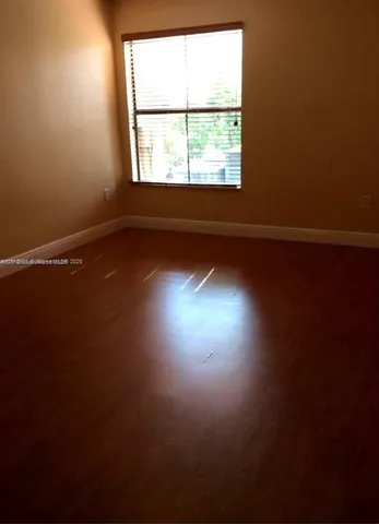 an empty room with wooden floor and windows with curtains