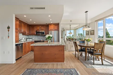 a kitchen with stainless steel appliances granite countertop a refrigerator a sink dishwasher a dining table and chairs with wooden floor