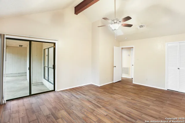 a view of an empty room with wooden floor and a ceiling fan