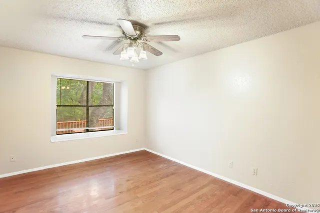 an empty room with wooden floor fan and windows