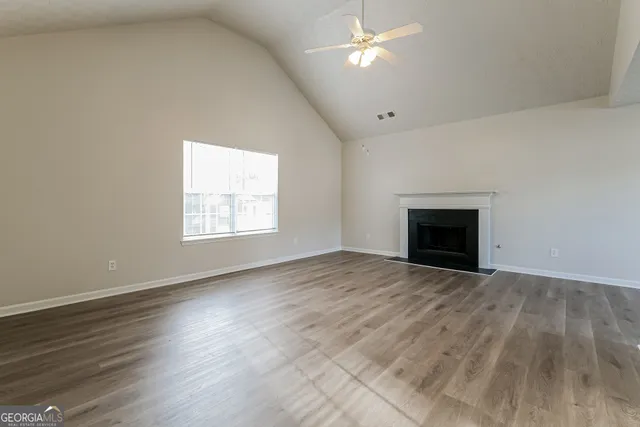 an empty room with wooden floor fan and windows