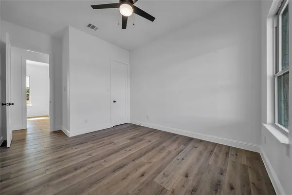 an empty room with wooden floor chandelier fan and windows