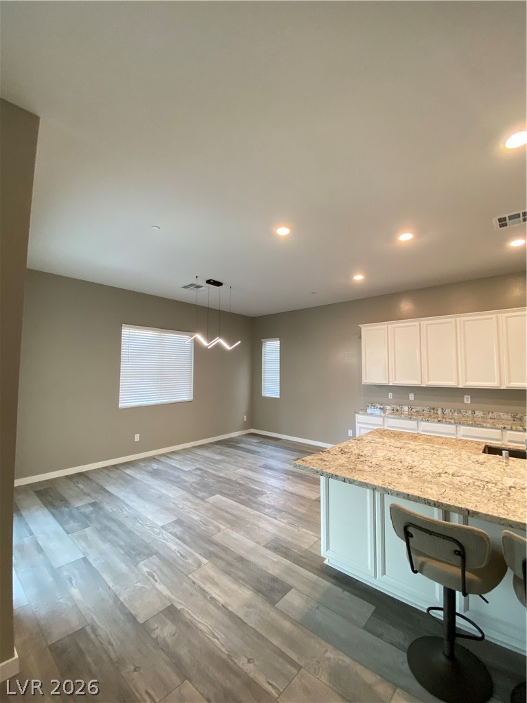695 Daylight Ridge Court Henderson, NV 89052 - Photo 3 of 27 Kitchen with pendant lighting, light stone counters, white cabinetry, dark wood-style floors, and a kitchen breakfast bar