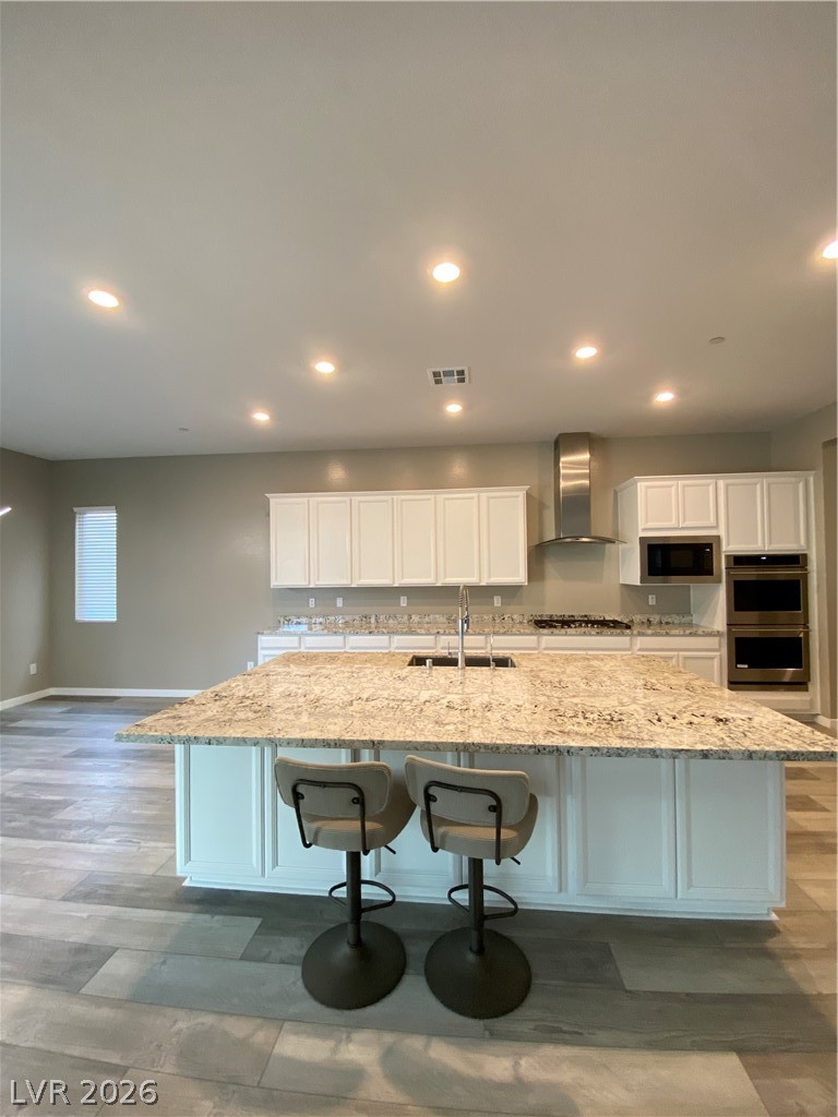 695 Daylight Ridge Court Henderson, NV 89052 - Photo 4 of 27 Kitchen with white cabinets, a kitchen bar, light wood-style flooring, light stone countertops, and recessed lighting