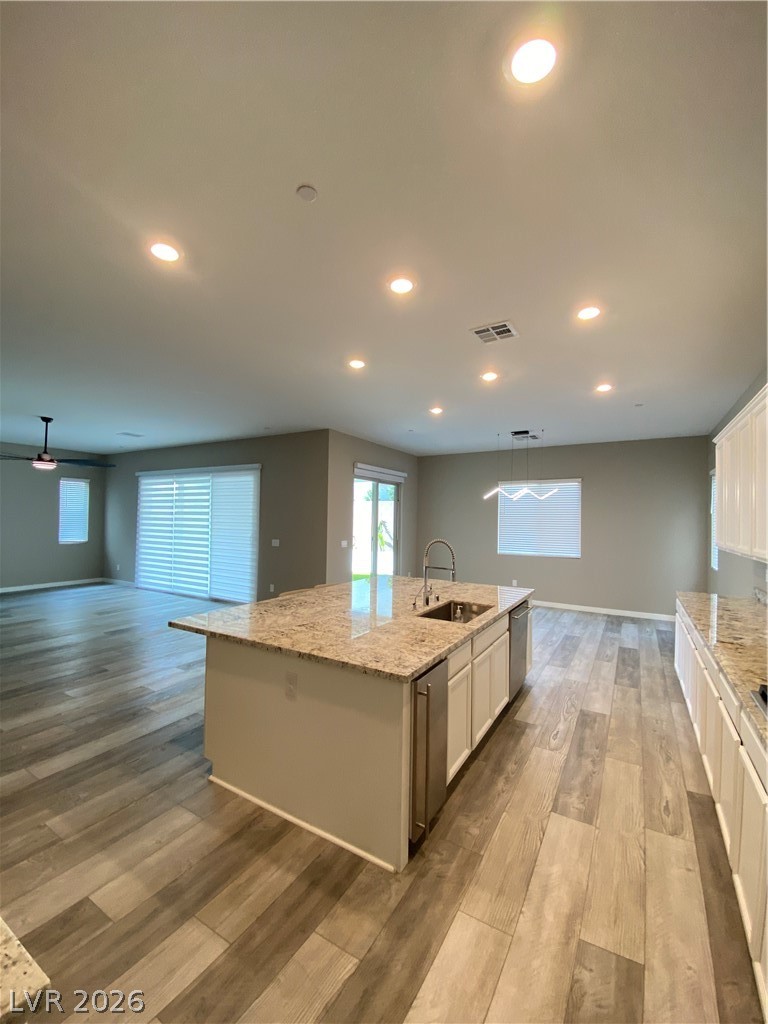 695 Daylight Ridge Court Henderson, NV 89052 - Photo 6 of 27 Kitchen with a center island with sink, light stone countertops, white cabinets, pendant lighting, and light wood finished floors