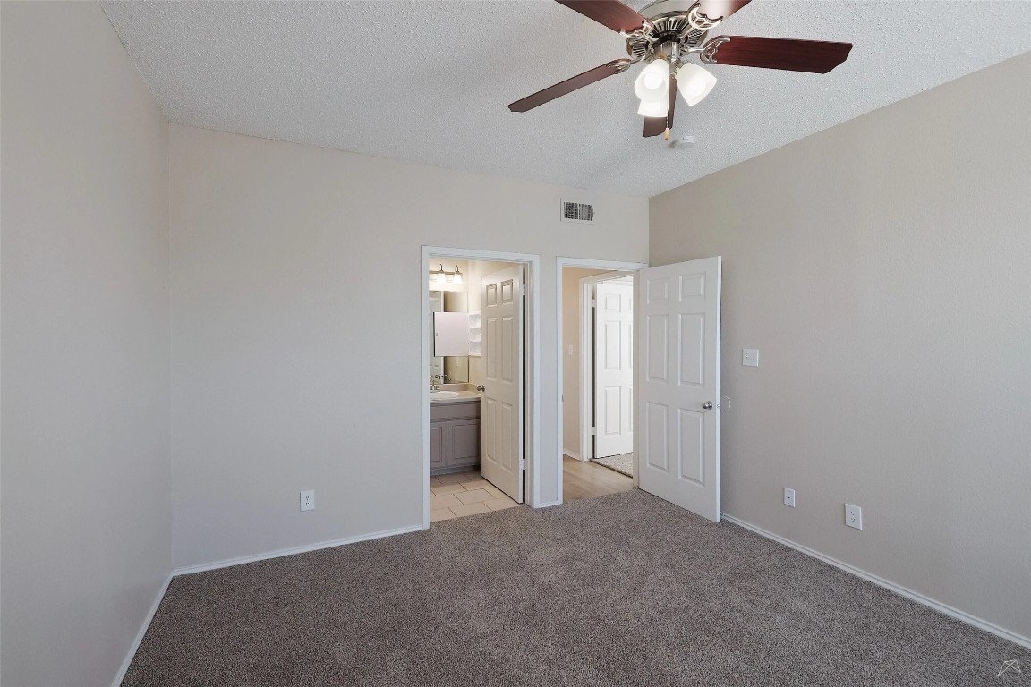 11908 Anderson Mill Road, Unit 1121 Austin, TX 78726 - Photo 15 of 24 Unfurnished bedroom featuring a textured ceiling, a ceiling fan, light carpet, and ensuite bath