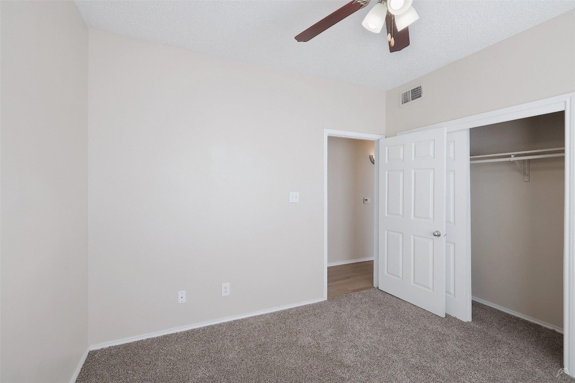 11908 Anderson Mill Road, Unit 1121 Austin, TX 78726 - Photo 23 of 24 Unfurnished bedroom featuring carpet flooring, a closet, a ceiling fan, and a textured ceiling
