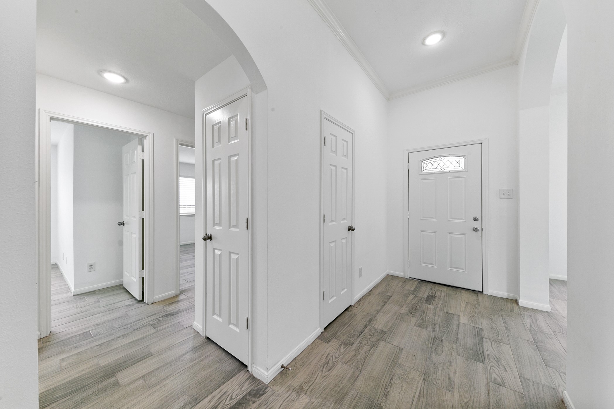 12014 Raven View Drive Houston, TX 77067 - Photo 6 of 29 Bright entry hallway with wood-look flooring, white walls, and recessed lighting. Features include a front door with decorative glass, arched entryways, and multiple interior doors leading to other rooms.