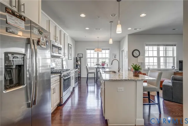a kitchen with stainless steel appliances kitchen island granite countertop a table chairs refrigerator and sink
