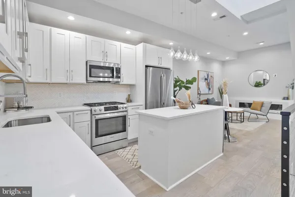 a kitchen with stainless steel appliances kitchen island granite countertop a stove a sink a refrigerator and white cabinets with wooden floor