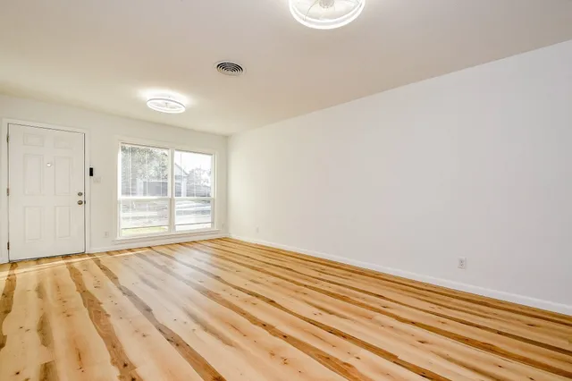 a view of an empty room with wooden floor and a window