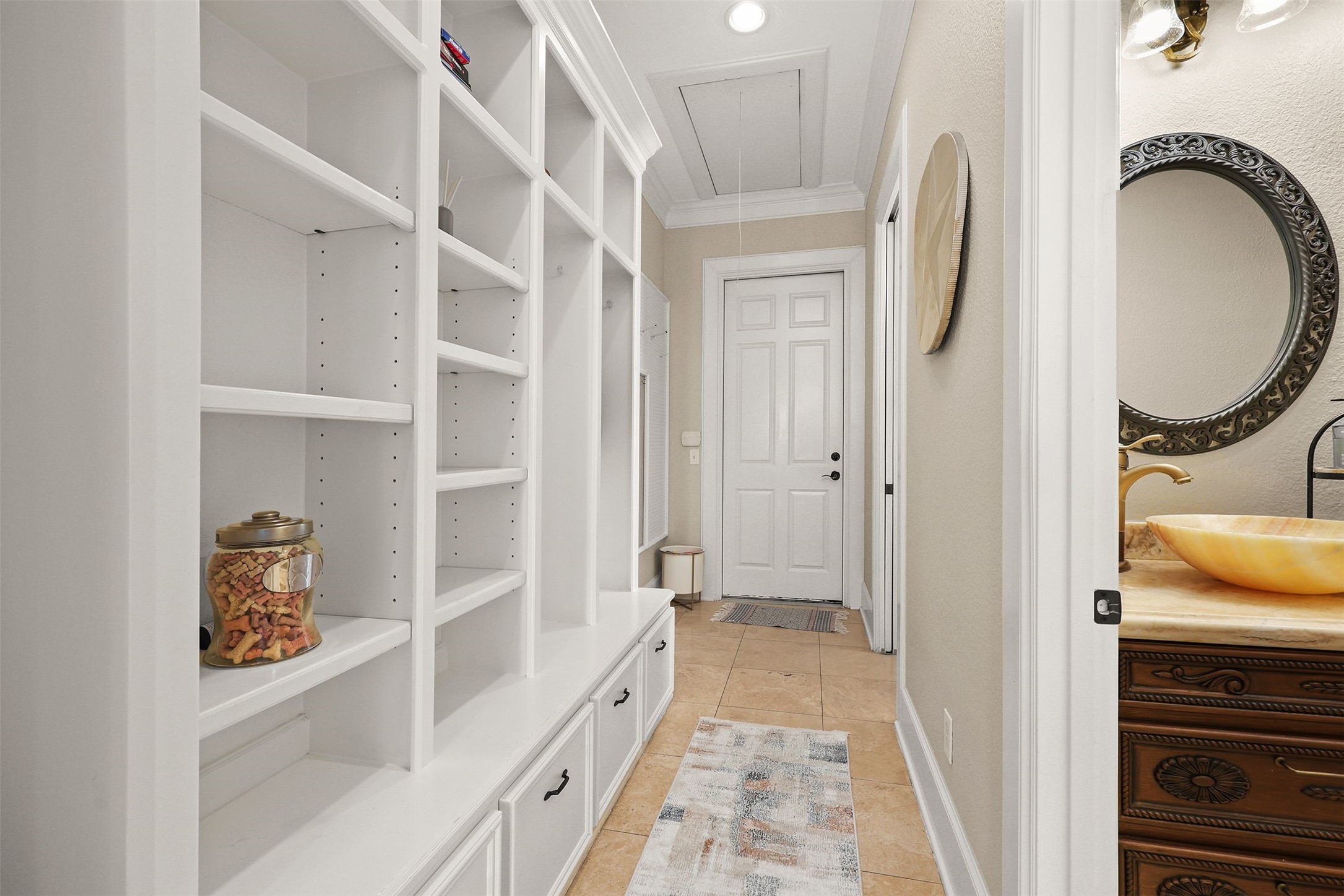 10896 Decatur Street Willis, TX 77318 - Photo 20 of 50 This well-lit hallway offers custom built-in shelving for ample storage, while a stylish bathroom with a vessel sink and ornate mirror adds elegance, creating a cozy and functional entryway or mudroom in neutral tones.