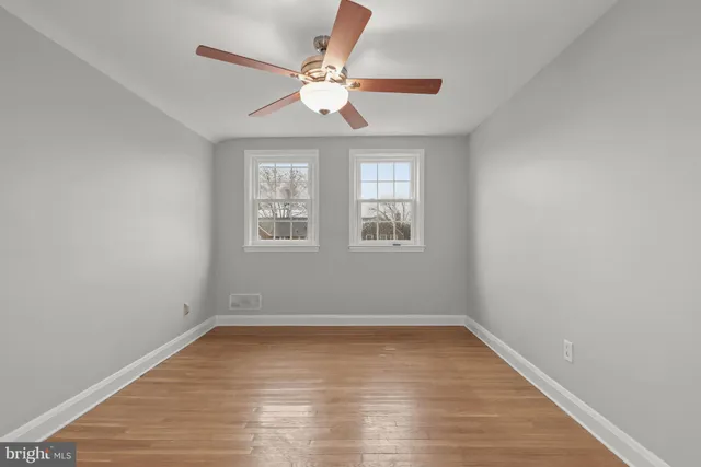an empty room with wooden floor fan and windows