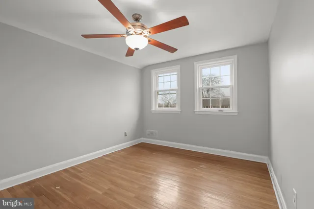 an empty room with wooden floor ceiling fan and windows