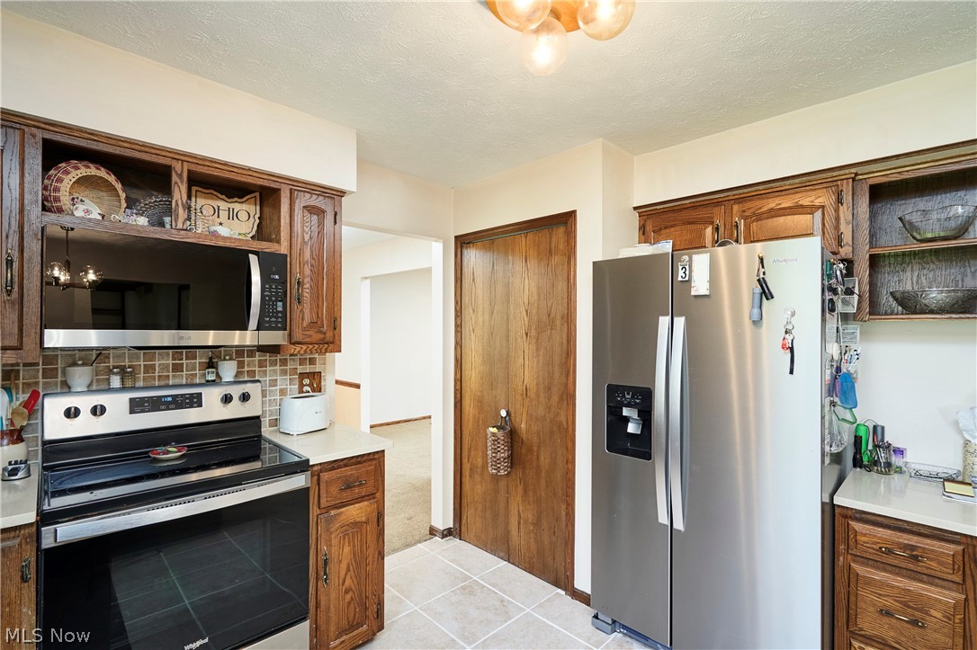 3097 Baughman Road Clinton, OH 44216 - Photo 6 of 27 Kitchen featuring wood cabinetry, stainless steel appliances including a side-by-side refrigerator, built-in microwave, and electric range, light-toned countertops, and a tiled backsplash
