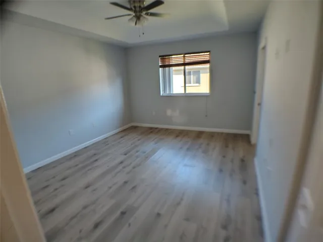 an empty room with wooden floor fan and windows