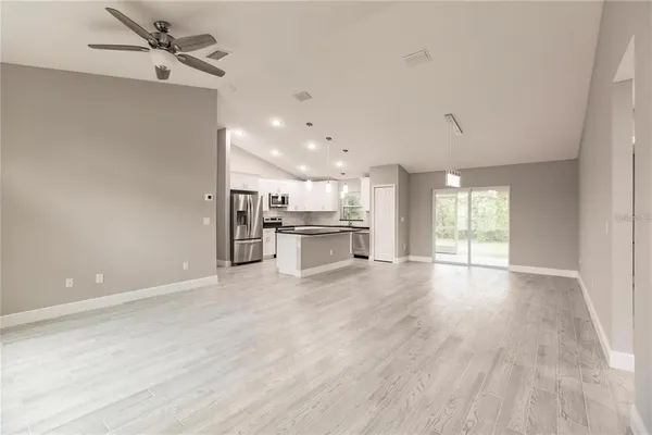 an empty room with wooden floor kitchen view and a window