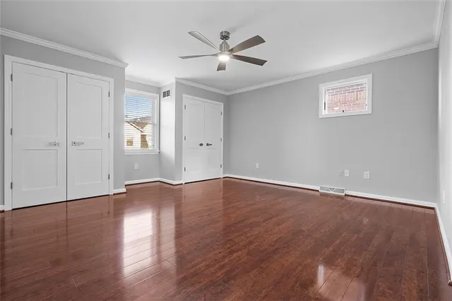 a view of an empty room with wooden floor and a ceiling fan