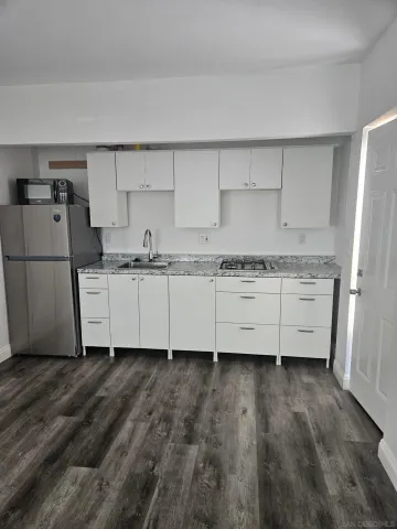 a kitchen with stainless steel appliances granite countertop a sink a stove a refrigerator with white cabinets and wooden floor