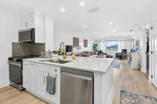 a kitchen with stainless steel appliances a sink a stove a refrigerator cabinets and a view of living room