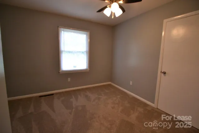 an empty room with a chandelier fan and windows