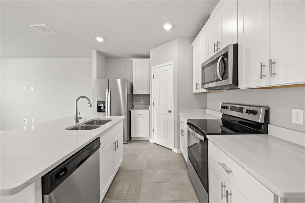 431 Legacy Loop Davenport, FL 33896 - Photo 7 of 25 a kitchen with stainless steel appliances granite countertop a sink stove a refrigerator and white cabinets with wooden floor