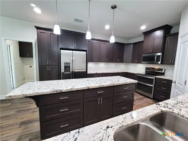 a kitchen with stainless steel appliances kitchen island granite countertop a refrigerator and a sink